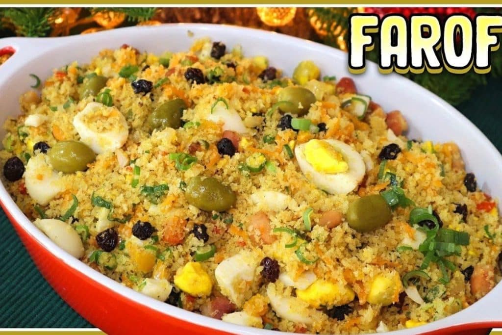 Farofa completa servida em uma travessa oval branca com bordas vermelhas. A farofa é colorida e apetitosa, contendo ovos cozidos, azeitonas, passas, cenoura ralada e cebolinha picada, misturados com a farinha torrada.