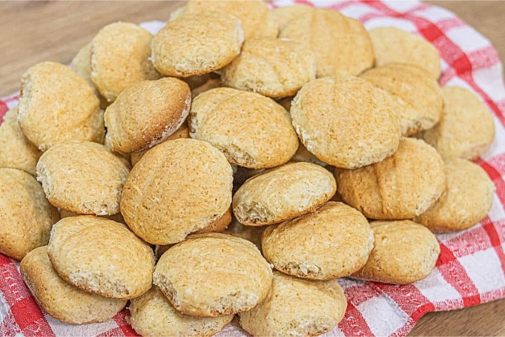 Biscoitos caseiros dourados empilhados sobre um pano de prato xadrez vermelho e branco, criando uma aparência aconchegante e rústica.