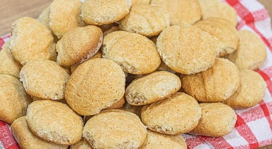 Biscoitos caseiros dourados empilhados sobre um pano de prato xadrez vermelho e branco, criando uma aparência aconchegante e rústica.