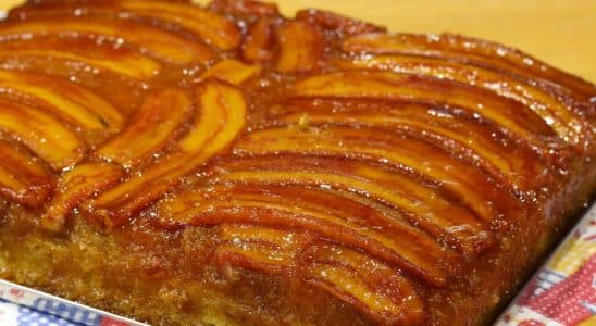 Bolo de banana caramelizada, servido em um prato retangular. O bolo tem uma camada de bananas caramelizadas no topo, criando uma aparência brilhante e apetitosa.