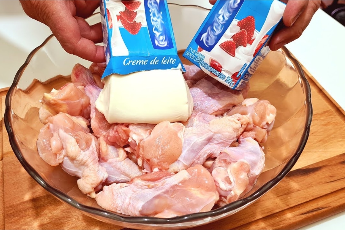 Frango com creme de leite sendo preparado, com pedaços de frango crus em uma tigela de vidro, e uma pessoa adicionando duas caixas de creme de leite.