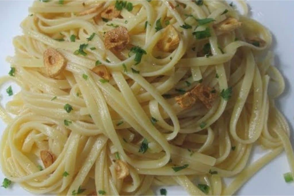 Macarrão alho e óleo, servido em um prato branco, decorado com fatias douradas de alho e salsa fresca picada, criando uma apresentação simples e elegante.