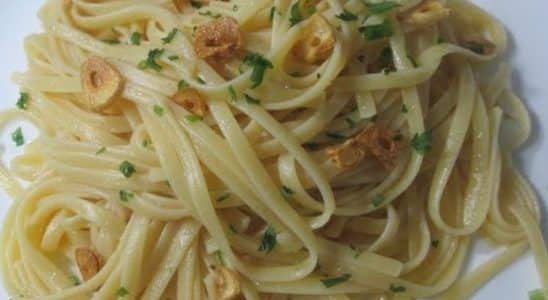 Macarrão alho e óleo, servido em um prato branco, decorado com fatias douradas de alho e salsa fresca picada, criando uma apresentação simples e elegante.