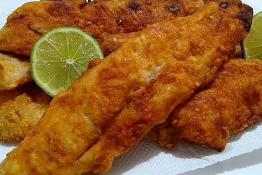 Peixe sequinho e crocante, empanado e frito, servido com rodelas de limão, em uma apresentação apetitosa e dourada.