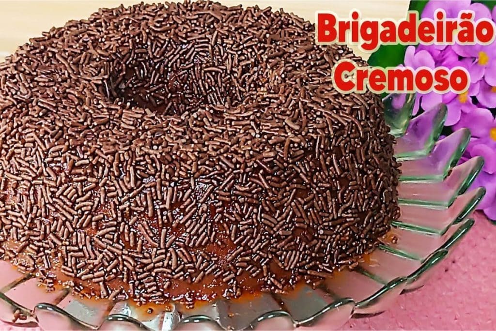 Brigadeirão cremoso, coberto com granulado de chocolate, servido em um prato de vidro.