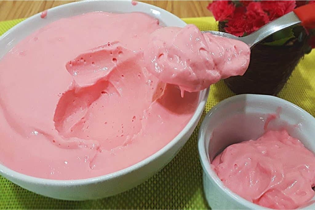 Mousse de morango, com uma textura leve e cremosa, servida em uma tigela branca. Uma colherada sendo retirada, mostrando a consistência suave e apetitosa.