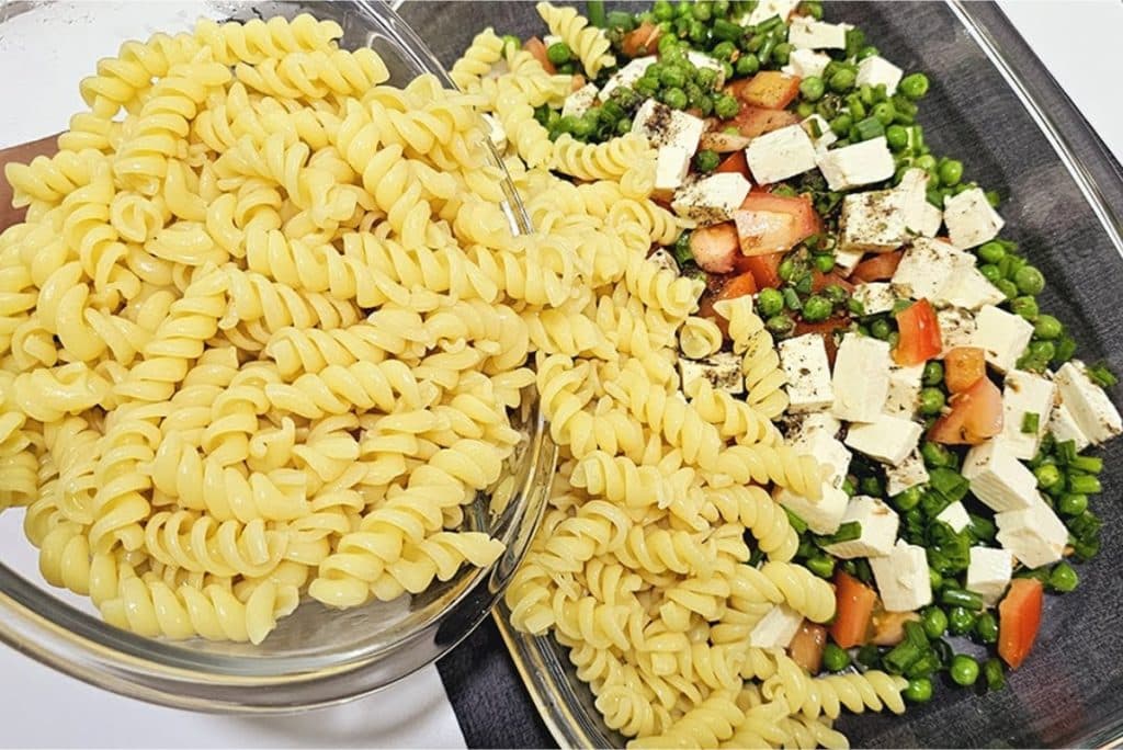 Salada de macarrão, com fusilli cozido e uma mistura colorida de ervilhas, tomates e cubos de queijo, apresentada em uma travessa de vidro. O prato exibe frescor e sabor, ideal para uma refeição leve e nutritiva.