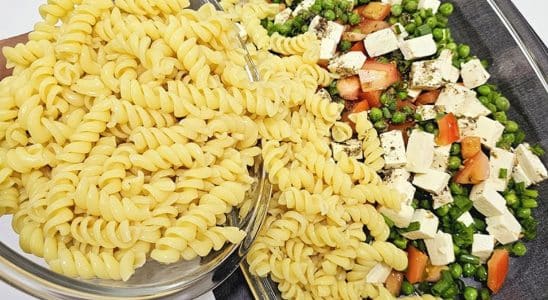 Salada de macarrão, com fusilli cozido e uma mistura colorida de ervilhas, tomates e cubos de queijo, apresentada em uma travessa de vidro. O prato exibe frescor e sabor, ideal para uma refeição leve e nutritiva.