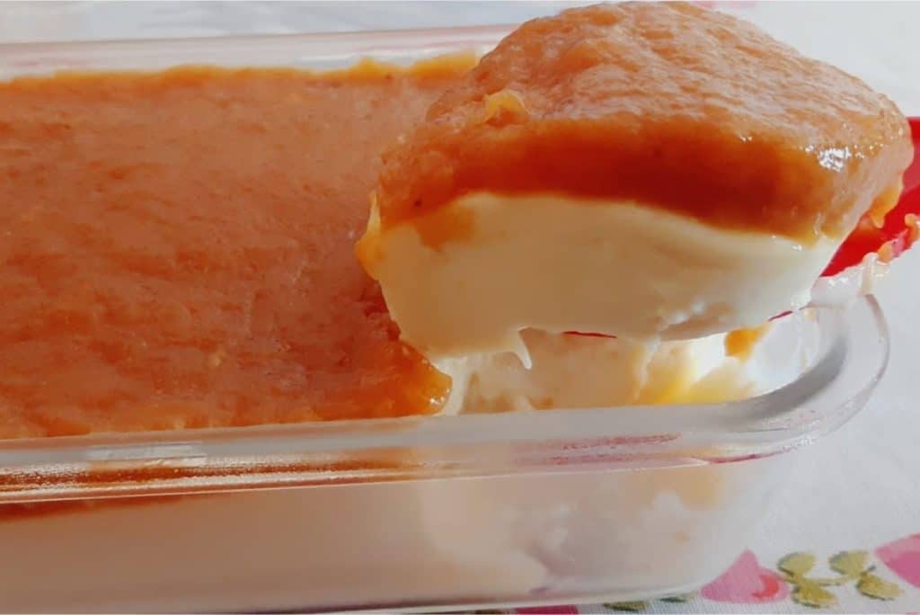 Sobremesa de banana caramelizada com creme de confeiteiro, servida em uma travessa de vidro. Uma colherada revela as camadas cremosas e a cobertura de banana caramelizada.