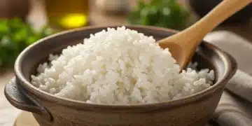 Arroz branco soltinho e perfeitamente cozido em uma tigela de cerâmica rústica, com uma colher de pau ao lado.
