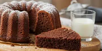 Bolo de chocolate com fermentação natural, fatiado, em uma tábua de madeira, com calda e frutas vermelhas por cima.