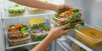 Pessoa organizando marmitas saudáveis e coloridas na geladeira, prontas para a semana, simbolizando a praticidade do cozimento em lotes.