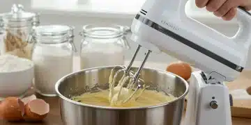 Batidora de mano moderna batiendo masa en un cuenco de acero inoxidable en una cocina luminosa.