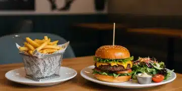 Close-up of a delicious plant-based burger with fresh toppings and sides in a stylish restaurant setting.