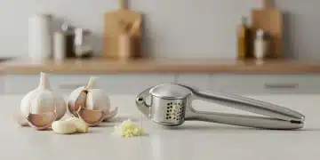 Prensa de ajos moderna de acero inoxidable sobre encimera, con ajos pelados y picados, destacando su diseño fácil de limpiar.