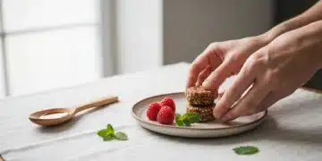 Woman's hands arranging a date-sweetened energy bite with fresh raspberries and mint on a rustic ceramic plate, embodying mindful indulgence in healthy desserts.