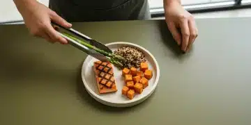 Overhead view of a woman arranging a healthy main dish with salmon, quinoa, asparagus, and sweet potatoes on a green plate, under soft natural light.