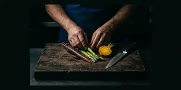 A chef's hand arranging raw heirloom vegetables on a wooden cutting board under dramatic spotlight, symbolizing expert plate building.