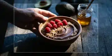 A person's hand holding a bowl of dark chocolate avocado mousse with raspberries, illustrating healthy dessert redefined beyond calories.